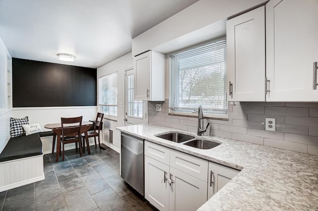 kitchen with light stone countertops, white cabinets, tasteful backsplash, sink, and stainless steel dishwasher