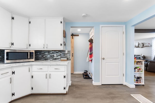 kitchen featuring white cabinets, backsplash, and a barn door