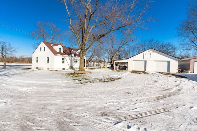 snow covered property with a carport, an outdoor structure, and a garage