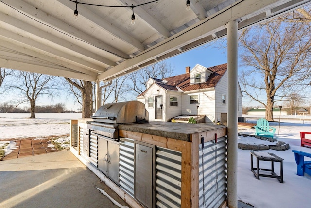 snow covered patio featuring grilling area and an outdoor kitchen