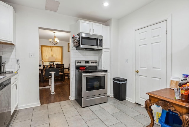 kitchen featuring an inviting chandelier, light tile patterned floors, appliances with stainless steel finishes, tasteful backsplash, and white cabinets