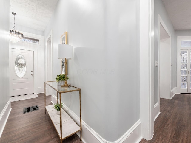 entryway featuring a textured ceiling, dark hardwood / wood-style flooring, and an inviting chandelier