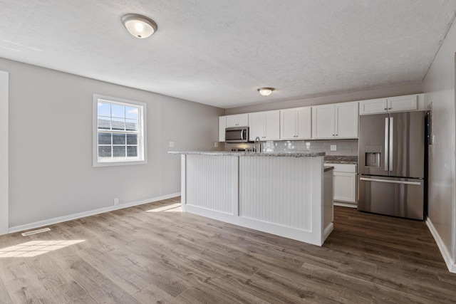 kitchen with tasteful backsplash, an island with sink, stainless steel appliances, and white cabinetry