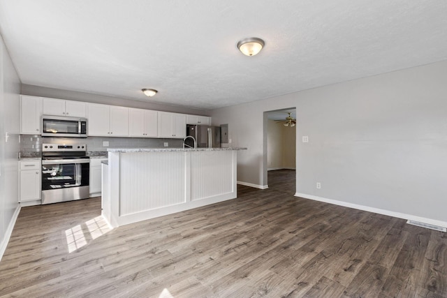 kitchen featuring hardwood / wood-style floors, a center island with sink, appliances with stainless steel finishes, white cabinets, and light stone counters