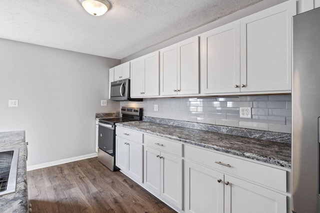 kitchen featuring white cabinetry, dark hardwood / wood-style flooring, stainless steel appliances, dark stone counters, and backsplash