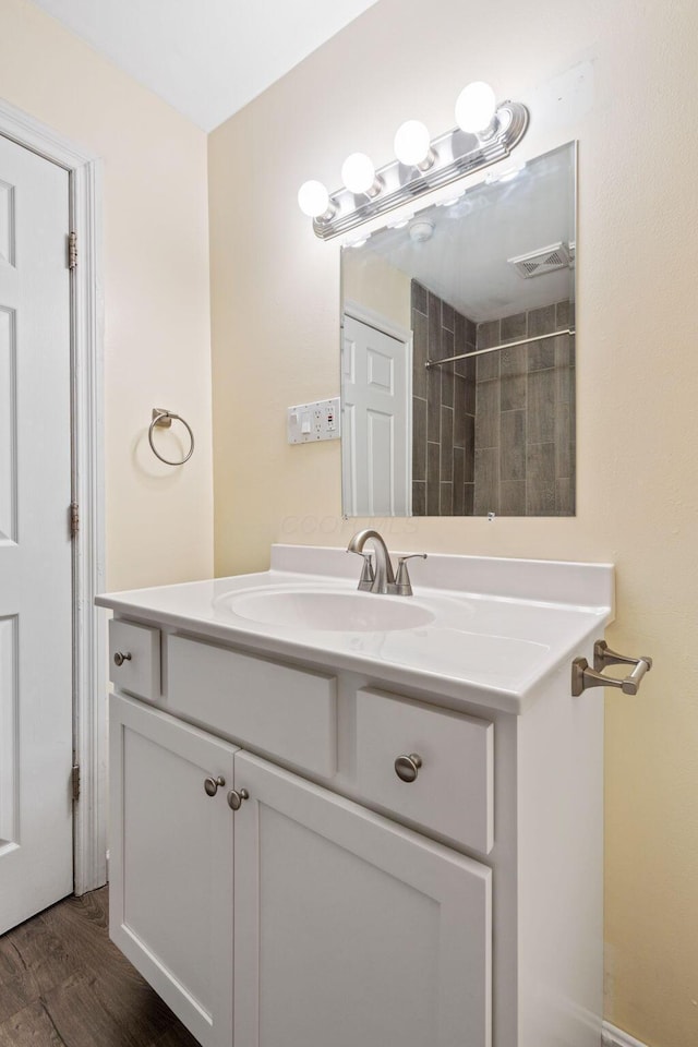 bathroom featuring wood-type flooring, tiled shower, and vanity