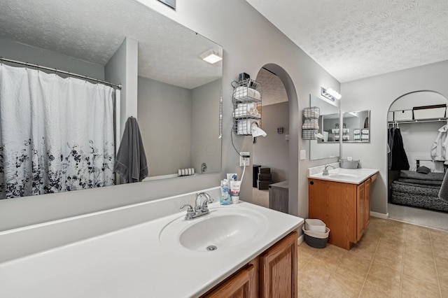 full bathroom with a textured ceiling, two vanities, a sink, and tile patterned flooring