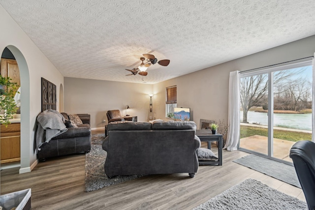 living room featuring a ceiling fan, arched walkways, a textured ceiling, and wood finished floors