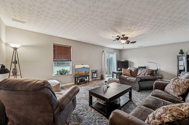 living area featuring baseboards, visible vents, a ceiling fan, wood finished floors, and a textured ceiling