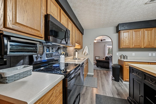 kitchen featuring arched walkways, light wood-type flooring, light countertops, black electric range, and a sink