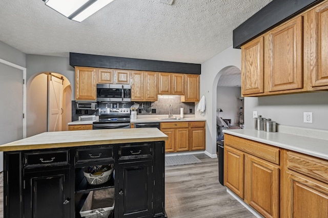 kitchen featuring arched walkways, dark cabinets, stainless steel appliances, light countertops, and light wood-type flooring