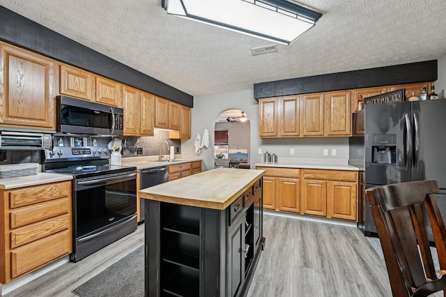 kitchen with arched walkways, light wood finished floors, visible vents, a sink, and black appliances