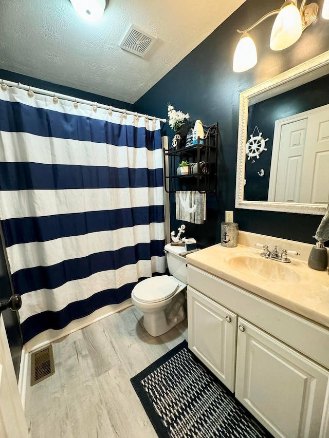 bathroom with a textured ceiling, lofted ceiling, wood-type flooring, vanity, and toilet