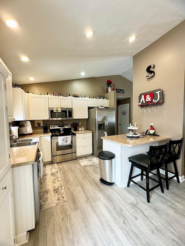 kitchen with lofted ceiling, a kitchen bar, sink, white cabinetry, and appliances with stainless steel finishes