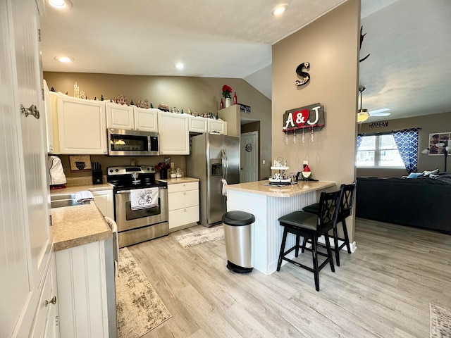 kitchen featuring appliances with stainless steel finishes, white cabinetry, light hardwood / wood-style floors, a kitchen breakfast bar, and vaulted ceiling