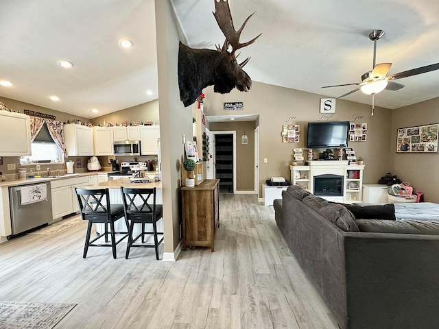 kitchen with lofted ceiling, white cabinetry, stainless steel appliances, ceiling fan, and light hardwood / wood-style flooring