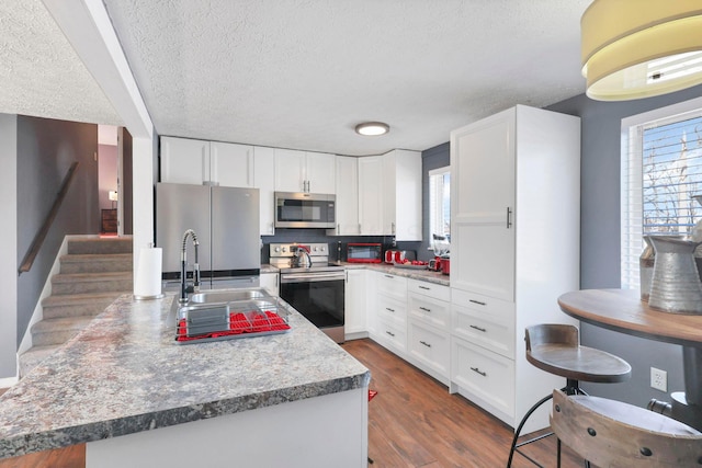 kitchen with stainless steel appliances, white cabinetry, dark hardwood / wood-style floors, and a textured ceiling