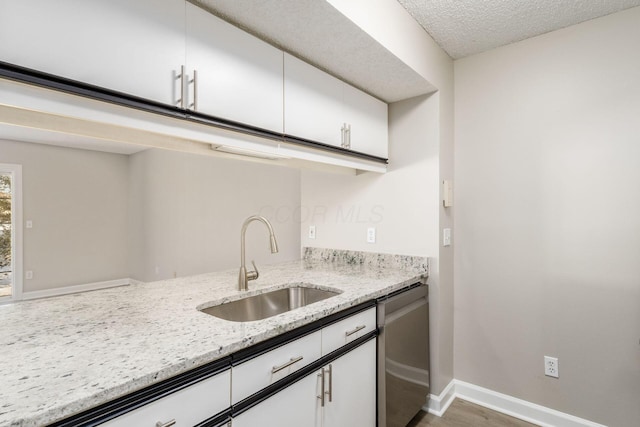 kitchen featuring light stone countertops, white cabinets, dishwasher, dark hardwood / wood-style flooring, and sink