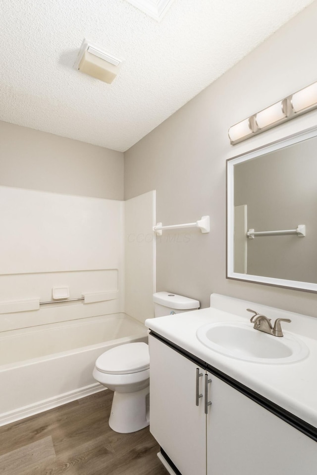 full bathroom featuring toilet, wood-type flooring, a textured ceiling, tub / shower combination, and vanity