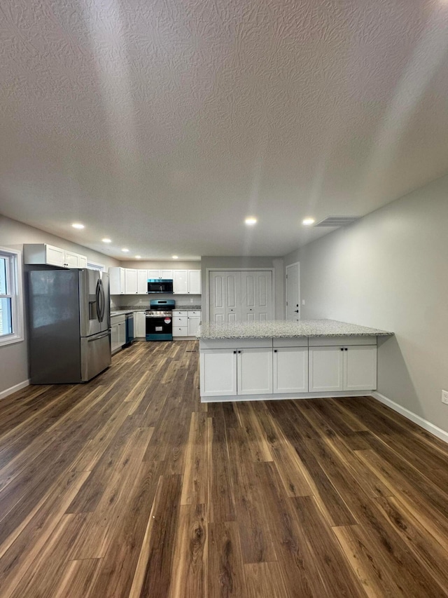 kitchen with appliances with stainless steel finishes, dark hardwood / wood-style floors, white cabinets, light stone counters, and kitchen peninsula