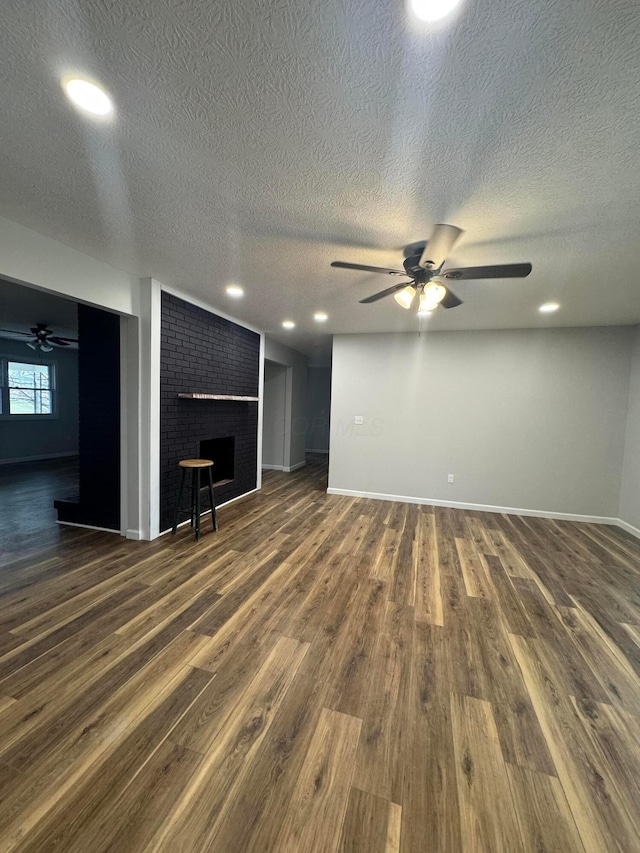 unfurnished living room featuring a brick fireplace, a textured ceiling, dark wood-type flooring, and ceiling fan