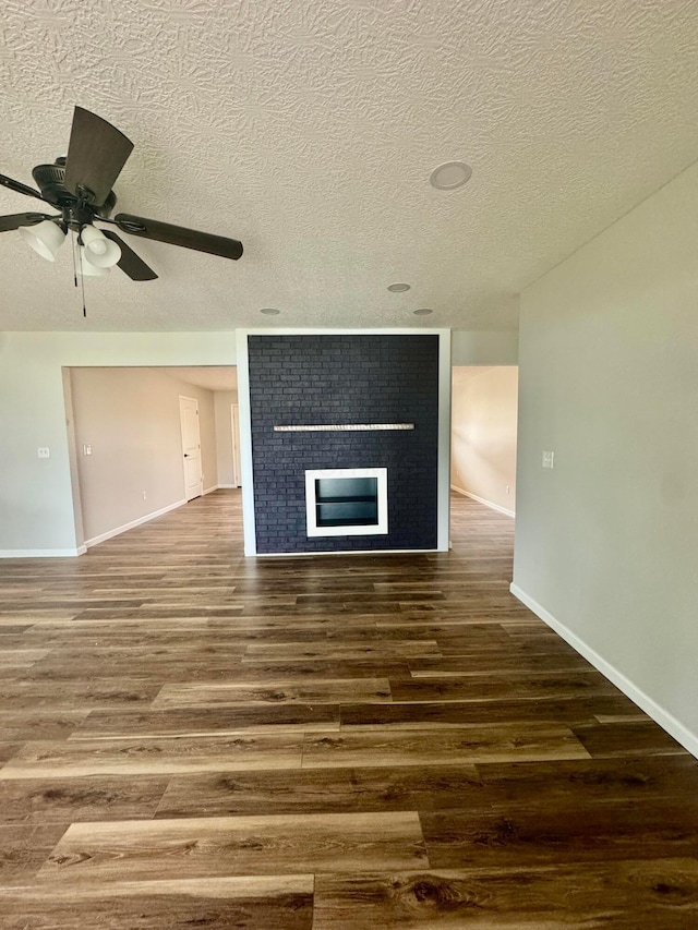 unfurnished living room with ceiling fan, a fireplace, dark hardwood / wood-style flooring, and a textured ceiling