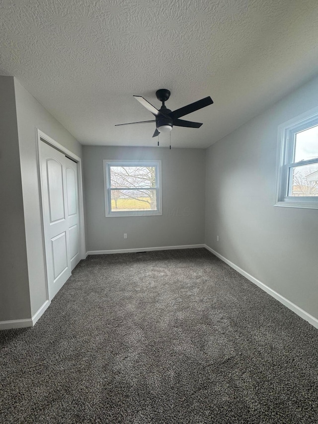 unfurnished bedroom with dark colored carpet, a textured ceiling, ceiling fan, and a closet