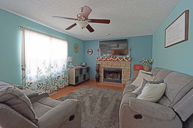 living room featuring ceiling fan, a fireplace, a textured ceiling, and hardwood / wood-style floors