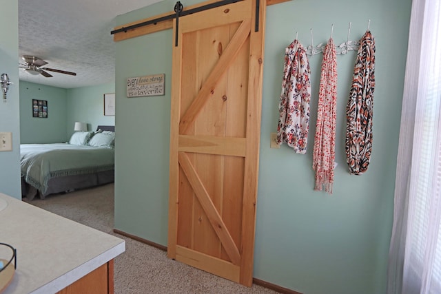 carpeted bedroom featuring a textured ceiling, ceiling fan, and a barn door