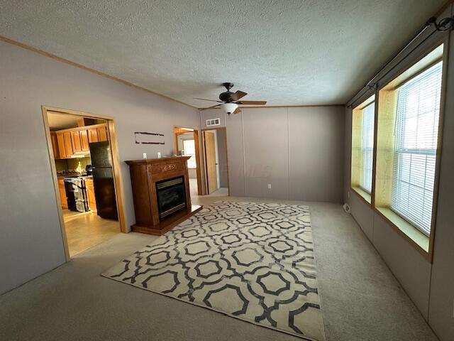 unfurnished living room with ceiling fan, a textured ceiling, and light carpet