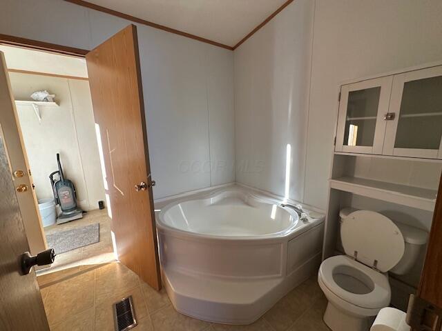 bathroom featuring toilet, tile patterned floors, ornamental molding, and a bath