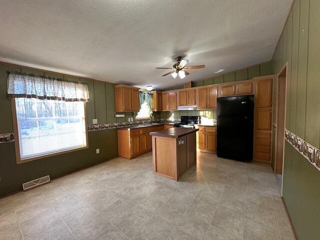 kitchen with ceiling fan, a kitchen island, black fridge, stove, and plenty of natural light