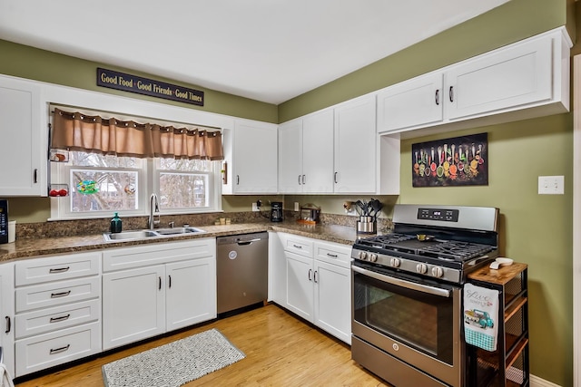 kitchen with white cabinetry, stainless steel appliances, light wood-type flooring, dark stone countertops, and sink