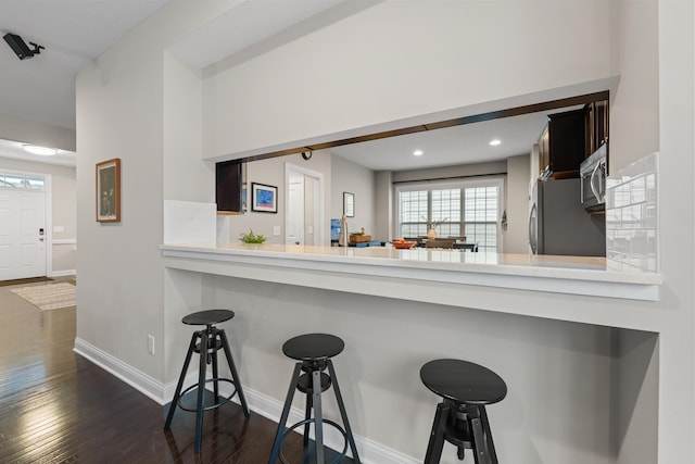 kitchen with dark wood-type flooring, appliances with stainless steel finishes, a kitchen bar, and kitchen peninsula