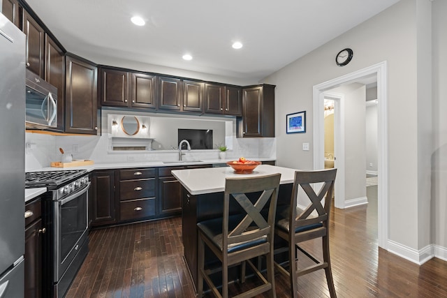 kitchen with a kitchen bar, appliances with stainless steel finishes, dark hardwood / wood-style floors, dark brown cabinets, and sink