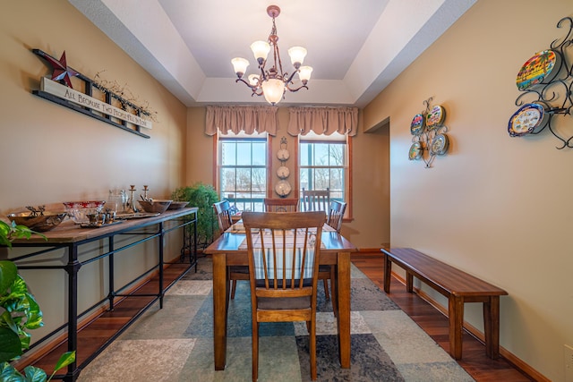 dining area with a tray ceiling, dark hardwood / wood-style floors, and a chandelier