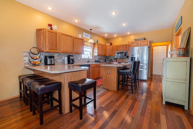 kitchen featuring a breakfast bar, hanging light fixtures, appliances with stainless steel finishes, dark hardwood / wood-style flooring, and kitchen peninsula