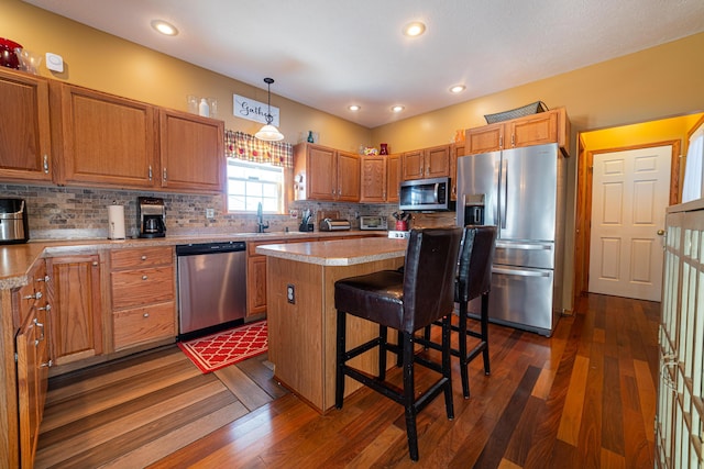 kitchen with sink, appliances with stainless steel finishes, hanging light fixtures, a center island, and a kitchen bar