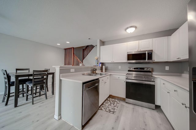 kitchen with kitchen peninsula, stainless steel appliances, white cabinets, and sink