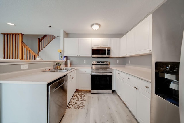 kitchen with white cabinets, stainless steel appliances, sink, kitchen peninsula, and light hardwood / wood-style flooring