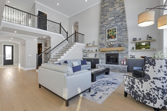 living room with ornamental molding, a stone fireplace, a towering ceiling, and light hardwood / wood-style floors