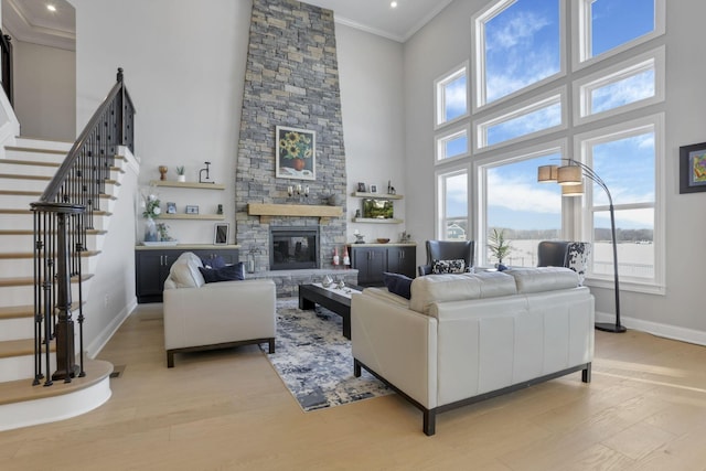 living room featuring crown molding, a towering ceiling, a fireplace, and light wood-type flooring