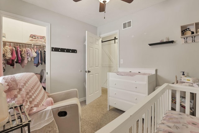 bedroom featuring a barn door, light carpet, ceiling fan, and a closet