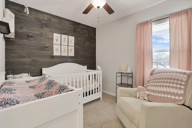 carpeted bedroom with a nursery area, ceiling fan, and wood walls