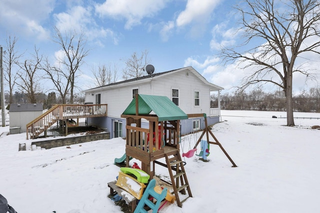 snow covered house featuring a wooden deck and a playground