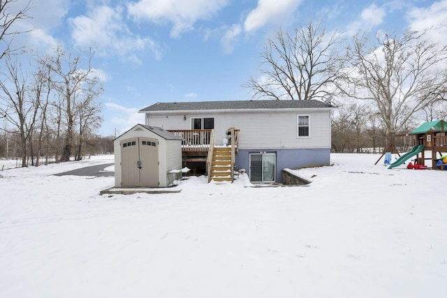 snow covered rear of property featuring a playground, a deck, and a storage shed