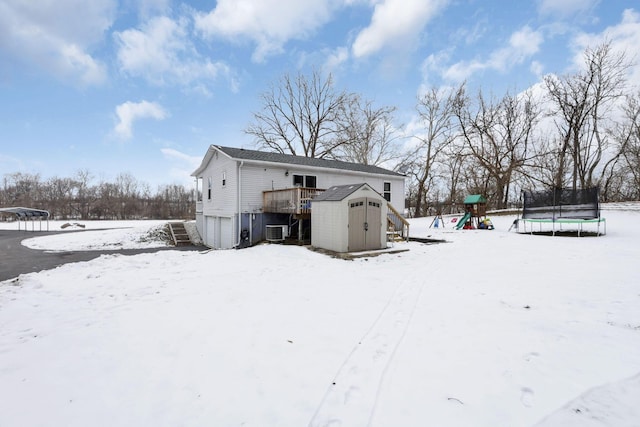 snow covered property with a playground, a storage unit, a wooden deck, a trampoline, and central AC unit