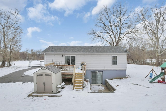 snow covered back of property featuring a storage shed, a playground, and a deck