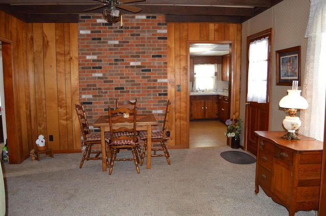 dining room with light colored carpet, beam ceiling, and wooden walls