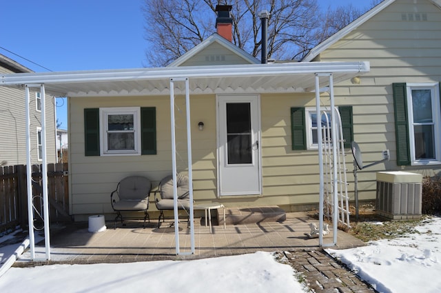 snow covered property entrance with central air condition unit and covered porch